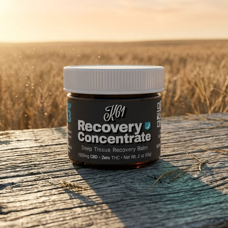 K61 Recovery Concentrate deep tissue balm jar on weathered wood beside a Kansas wheat field at sunset