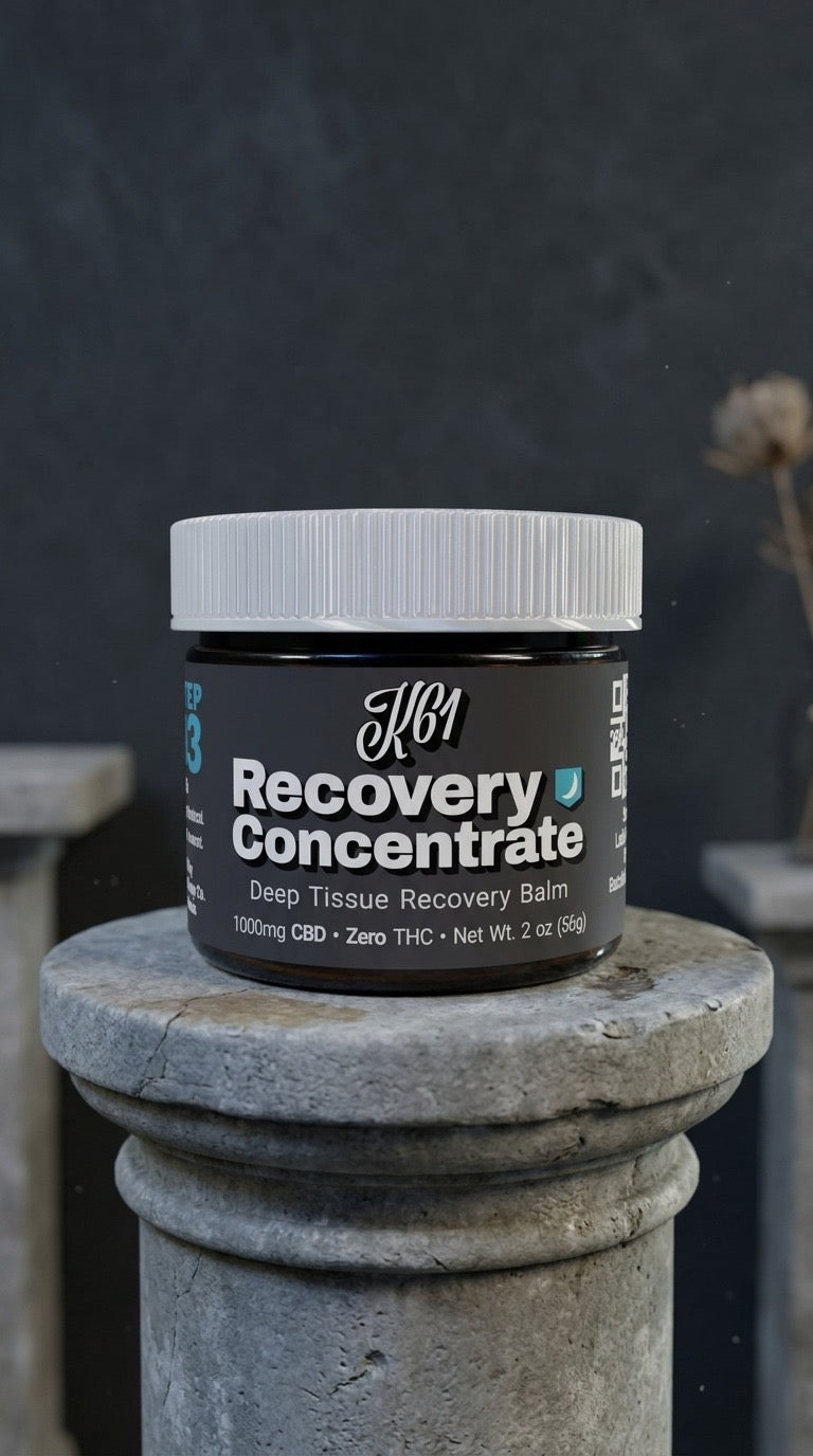 K61 Recovery Concentrate deep tissue balm jar on a grey stone pedestal against a charcoal wall, 1000mg CBD, Zero THC