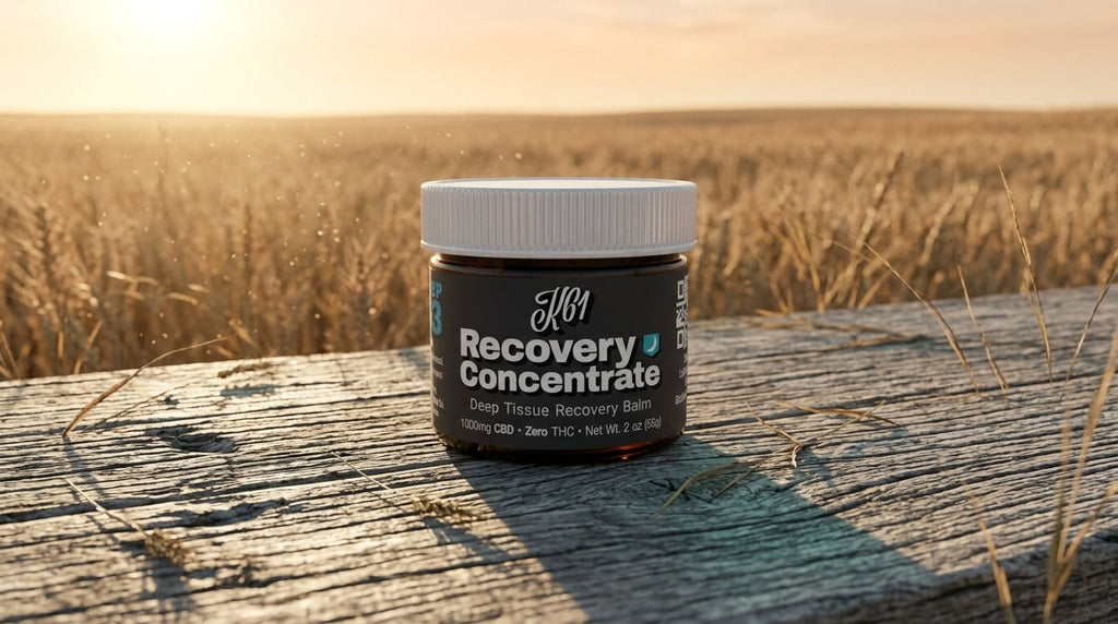 K61 Recovery Concentrate deep tissue balm jar on weathered wood beside a Kansas wheat field at sunset