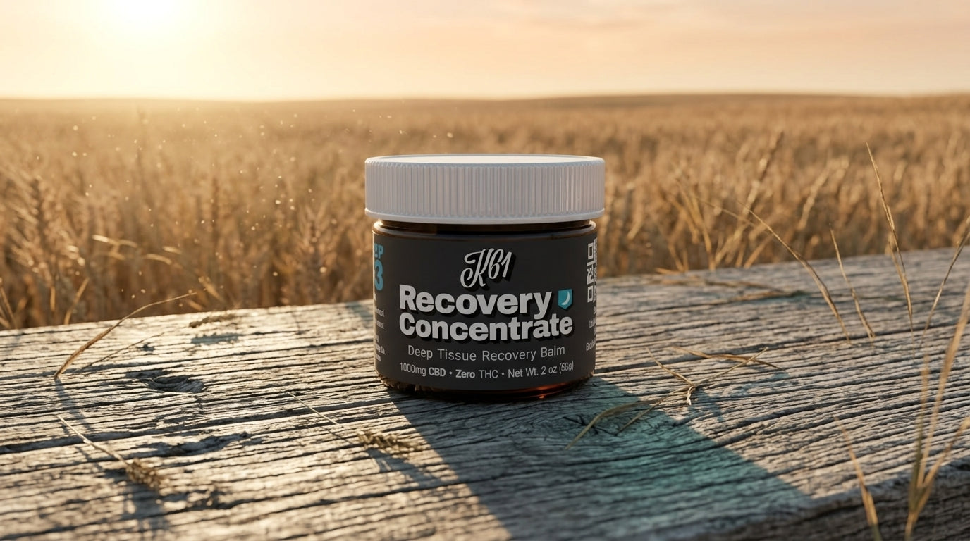 K61 Recovery Concentrate deep tissue balm jar on weathered wood beside a Kansas wheat field at sunset