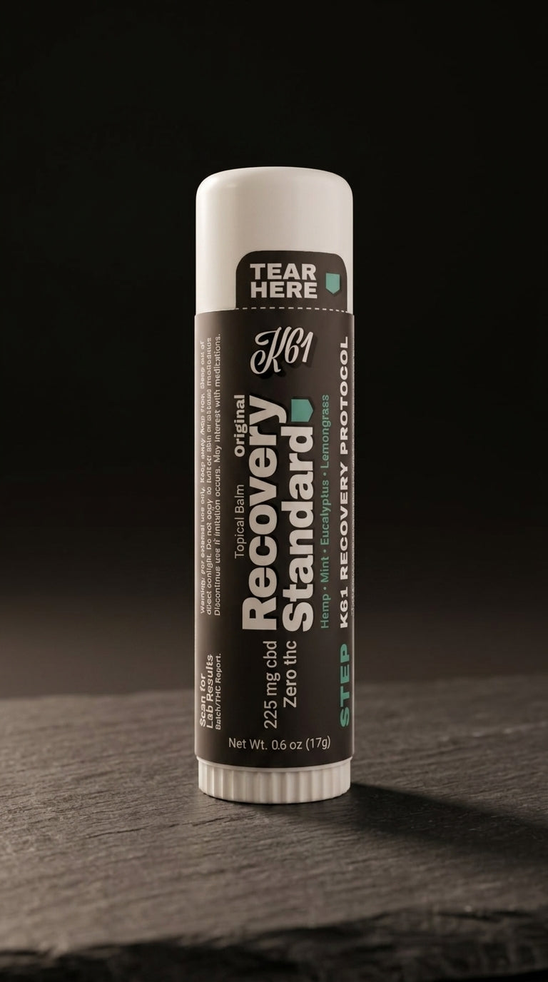 K61 Recovery Standard balm stick on charcoal slate, label showing 225mg CBD and Zero THC